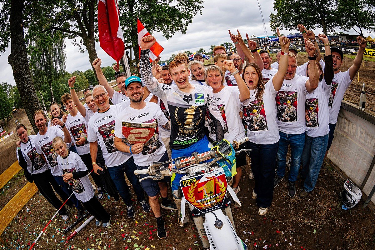 Skovbjerg sitzt freudig auf seinem Motorrad, und um ihn herum steht sein Team.