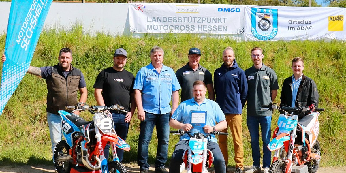 Gruppe von Personen vor dem Banner „Landesstützpunkt Motocross Hessen“ beim MSC Sechshelden, mit drei Motocross-Motorrädern im Vordergrund.