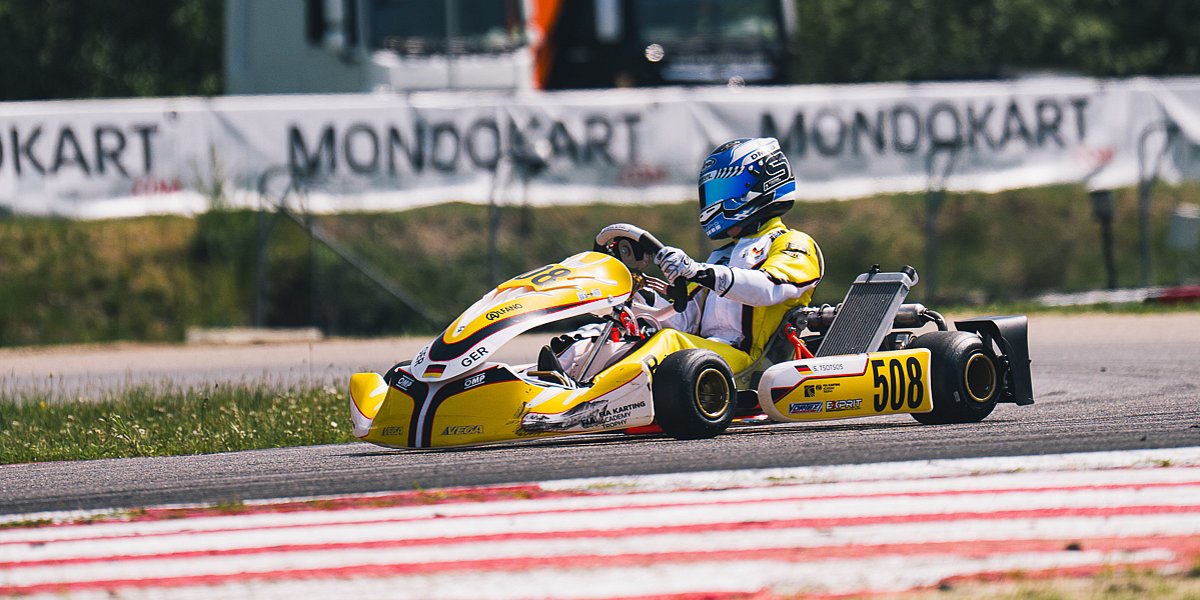 Stavros Tsotsos Francia, FIA Karting Academy Trophy Junior, Genk 2026 Stavros Tsotsos Francia fährt im gelben Kart durch eine Kurve der FIA Karting Academy Trophy, im Hintergrund sind MONDOKART-Banner und Transportfahrzeuge zu sehen.