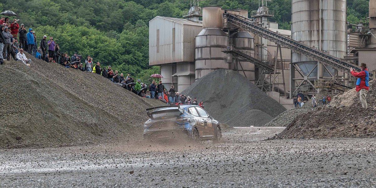 Hunsrück Rallye 2024 Ein Rallyefahrzeug fährt in einer Schotterkurve auf der Rennstrecke bei der Hunsrück Rallye 2024. Am Rand Zuschauer und ein Fotograf.