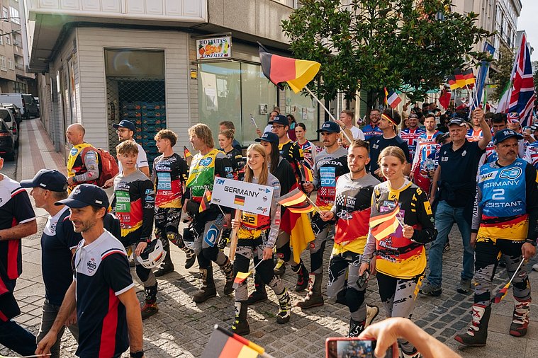 FIM Trial der Nationen (TdN) 2026, Arteixo Deutsches Trial-Team zieht mit ihren Landesflaggen durch die Straßen, begleitet von Teammitgliedern und Zuschauern beim Trial der Nationen.
