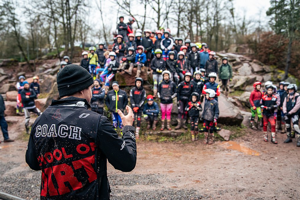 Trainer vor großer Gruppe Trialfahrern im Hintergrund