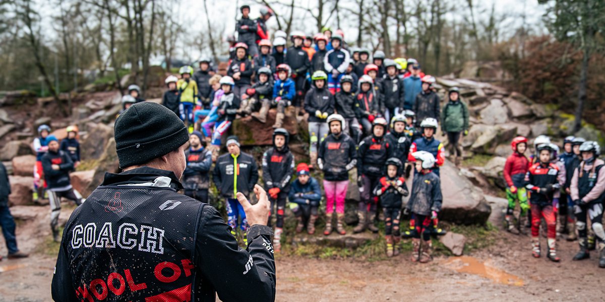 Trainer vor großer Gruppe Trialfahrern im Hintergrund