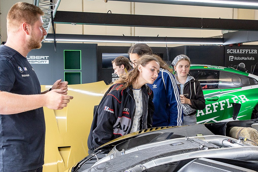 Ein Mechaniker erklärt einer Gruppe von Teilnehmerinnen die Technik eines DTM-Autos in der Schubert-Motorsport-Garage.