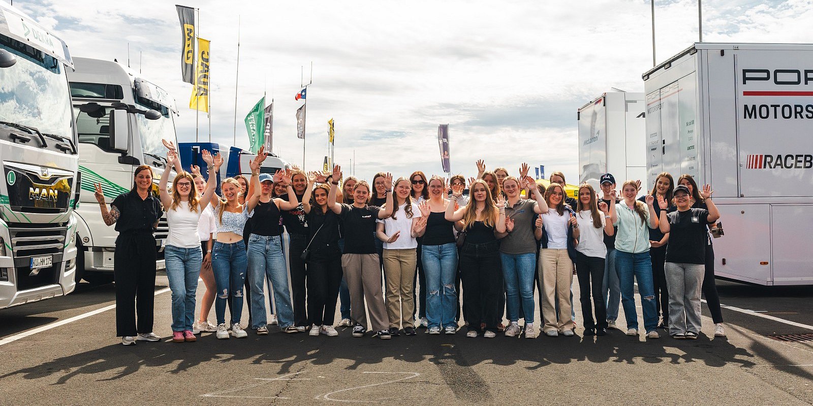 Discover Motorsport – Young Women’s Edition 2025 Gruppenfoto von Teilnehmerinnen der Discover Motorsport – Young Women’s Edition 2025 am Nürburgring mit erhobenen Händen vor den DTM-Teamtruckern, dazu das Event-Logo und der Hinweis „Am 23. Juli in Oschersleben – jetzt anmelden“.