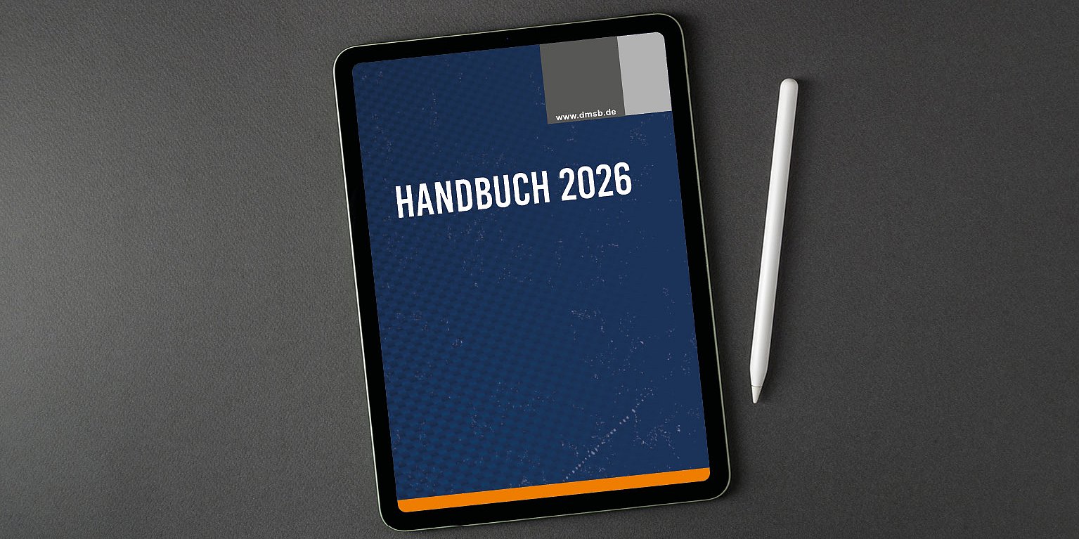 Ein Tablet, auf dessen Bildschirm HANDBUCH 2026 angezeigt wird, neben einem weißen Stift auf einer dunklen Fläche.