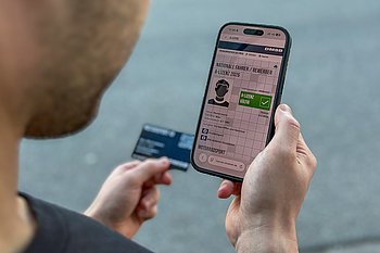 Kiesuntergrund, davor eine Hand, die eine Smartphone hält, darauf eine digitale Lizenz zu sehen.