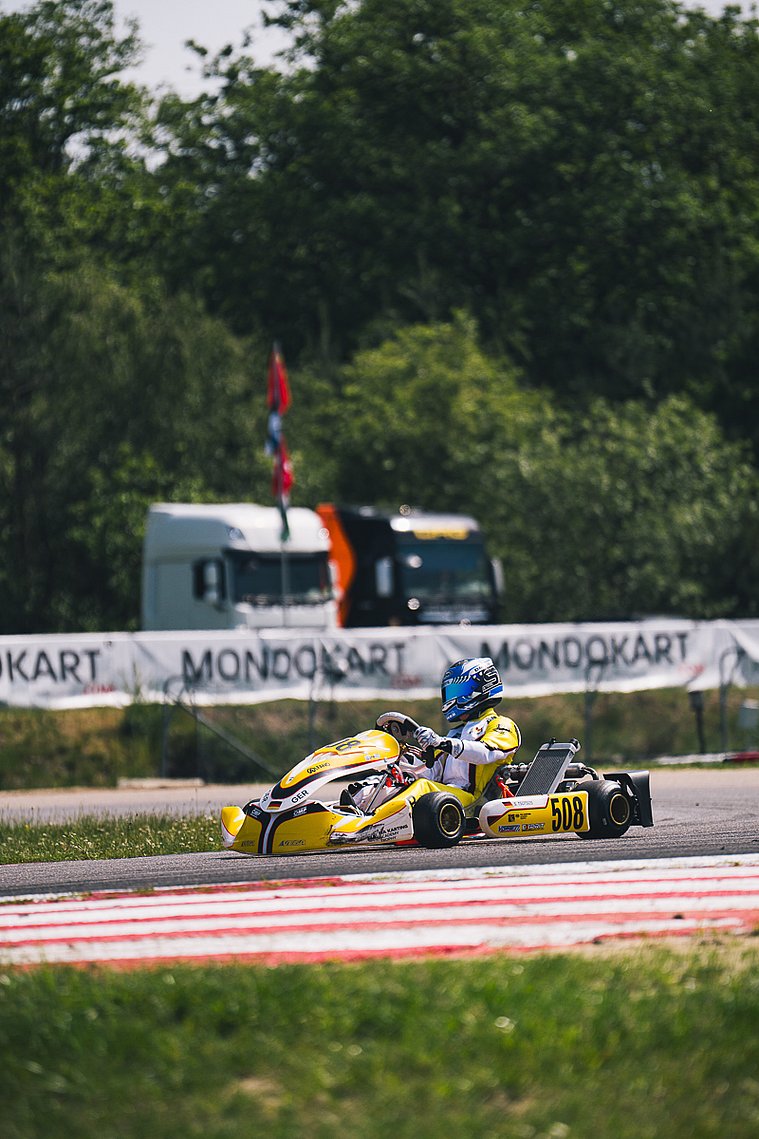 Stavros Tsotsos Francia, FIA Karting Academy Trophy Junior, Genk 2026 Stavros Tsotsos Francia fährt im gelben Kart durch eine Kurve der FIA Karting Academy Trophy, im Hintergrund sind MONDOKART-Banner und Transportfahrzeuge zu sehen.