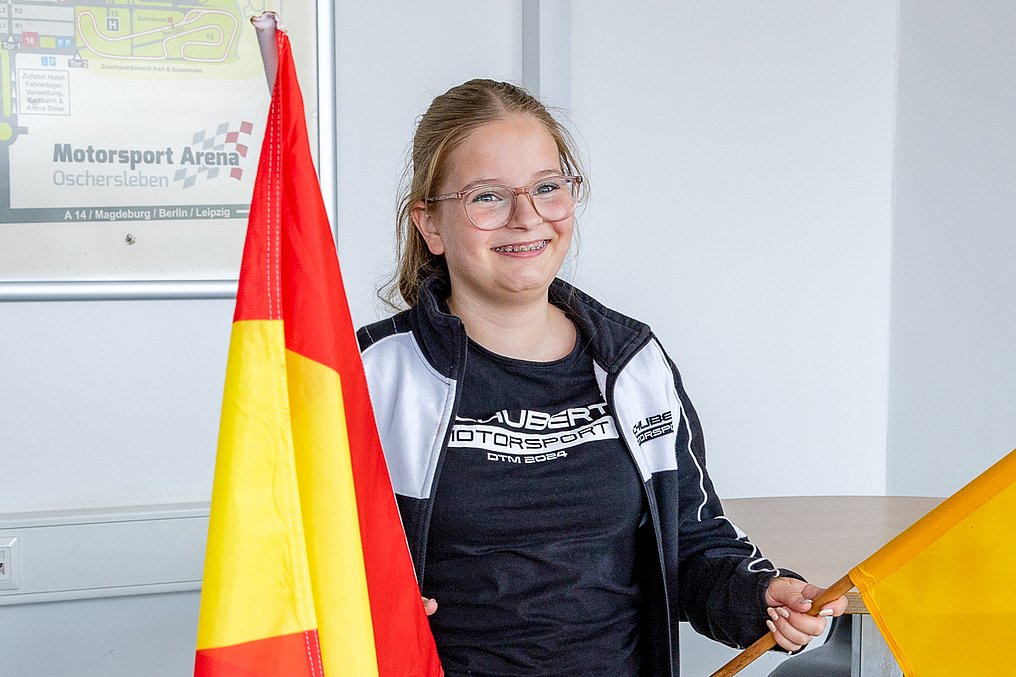 Eine Teilnehmerin hält bei den Sportwarten der Streckensicherung eine rot-gelbe Flagge und eine gelbe Flagge und lächelt in die Kamera.