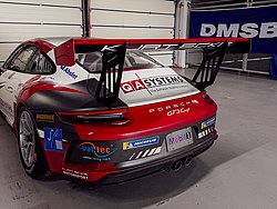 DMSB Medical Days 2026 DMSB Medical Days 2026: Roter Porsche GT3 Cup Rennwagen mit Sponsorenaufklebern in einer Garage, im Hintergrund ein DMSB-Banner.