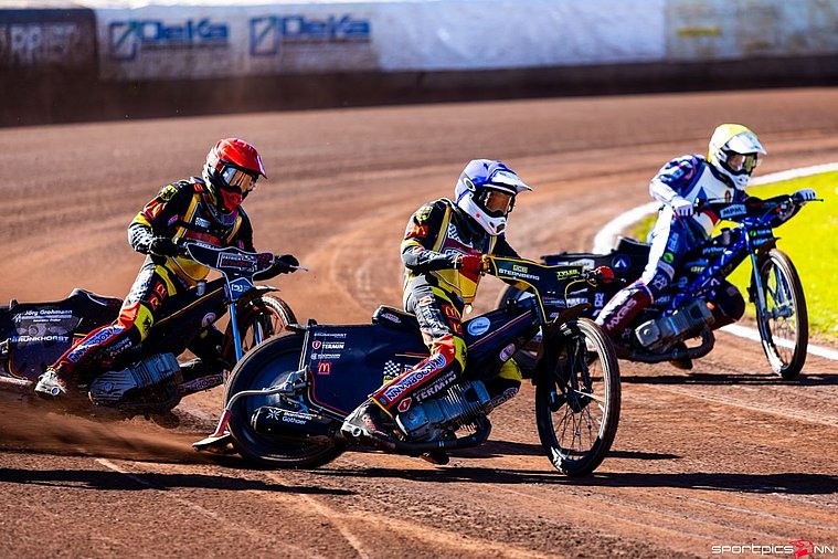 European U19 Pairs Speedway Championship Final 2026, Pocking Zwei deutsche Speedway-Fahrer im schwarz-rot-gelben Rennanzug fahren in einer Kurve auf der Sandbahn vor einem blau-weiß gekleideten Konkurrenten aus Tschechien.