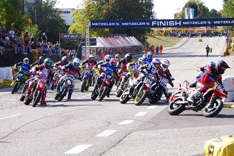 SuperMoto of Nations 2026, St. Wendel Supermoto-Fahrer verschiedener Nationen biegen auf einer Rennstrecke gemeinsam in die erste Kurve ein.