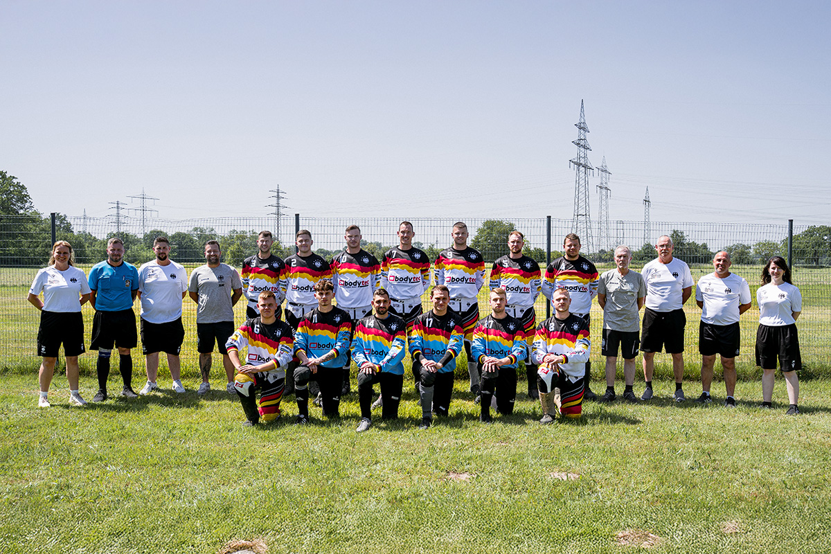 Motorsport Team Germany Motoball Senioren für die Motoball-EM 2026 Aufreihung des Motorsport Team Germany Motoball, 2 Reihen Personen mit deutschen Motoball Trickots stehen bzw. knien auf einer grünen Wiese unter freiem Himmel und schauen in die Kamera
